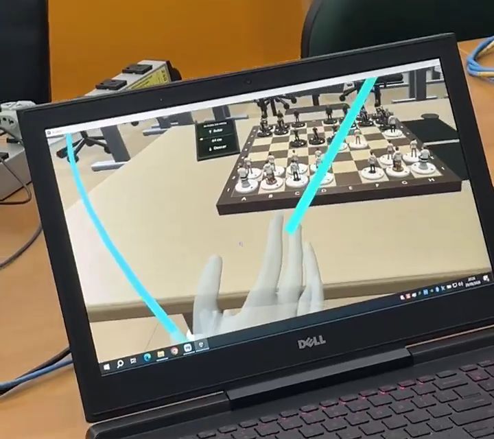 Visão do VR no notebook: mãos virtuais diante do tabuleiro dentro da sala.